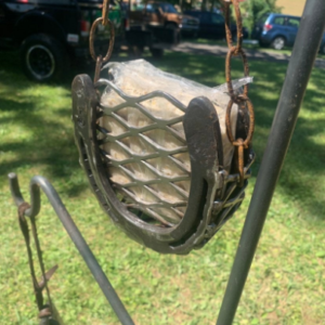 Handcrafted suet cake bird feeder made from horseshoes and chain, showcasing a suet cake inside, hanging in an outdoor setting.