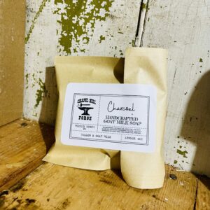 A bar of cleansing charcoal soap with goat milk and tallow, displayed against a rustic background.