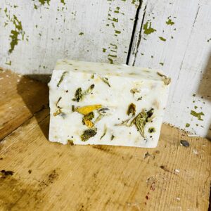 A bar of aromatherapy soap with preserved flowers, peony essential oil, goat milk, and tallow, displayed against a soft, natural backdrop.