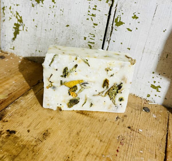 A bar of aromatherapy soap with preserved flowers, peony essential oil, goat milk, and tallow, displayed against a soft, natural backdrop.