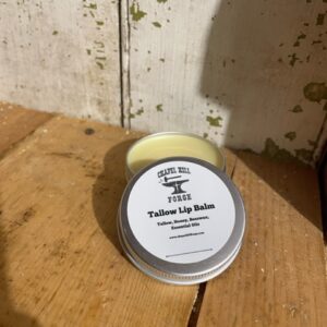 A tin of tallow lip balm with simple ingredients, displayed against a neutral background.