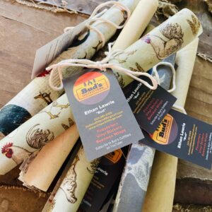 Beeswax wraps laid out on a wooden surface, showcasing their natural texture and various sizes, made from local beeswax, cotton fabric, jojoba oil, and pine tar resin.