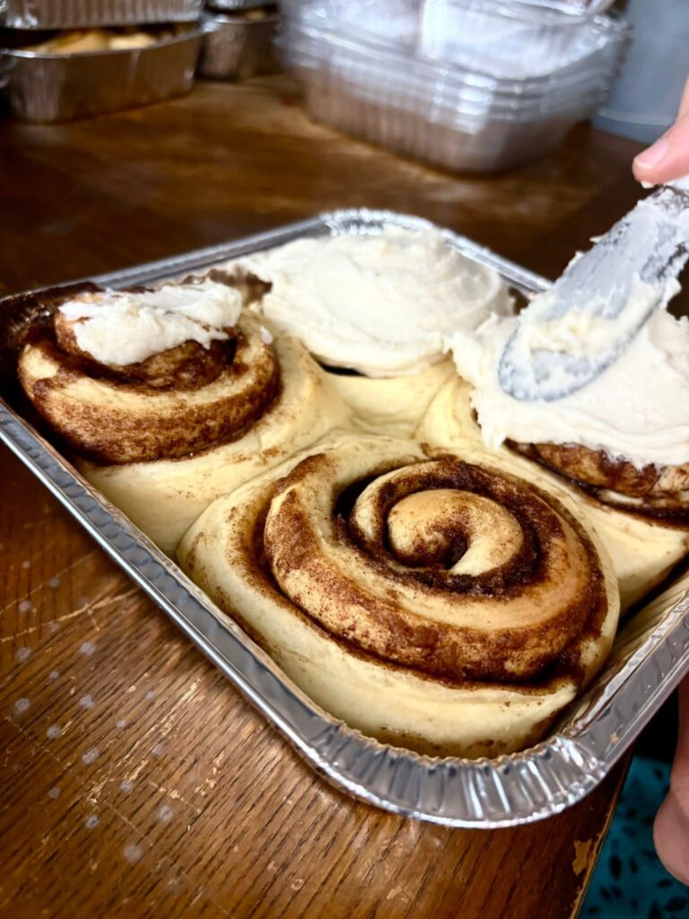 Micro bakery carefully icing a fresh batch of cinnamon rolls in a cozy home kitchen.