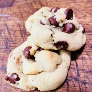 Freshly baked soft and chewy chocolate chip cookies resting on a wooden cutting board, with golden edges and melted chocolate chips visible.