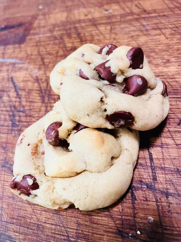 Freshly baked soft and chewy chocolate chip cookies resting on a wooden cutting board, with golden edges and melted chocolate chips visible.